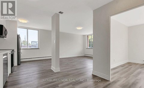 A realtor photo of a large empty room with wood floors and white walls.