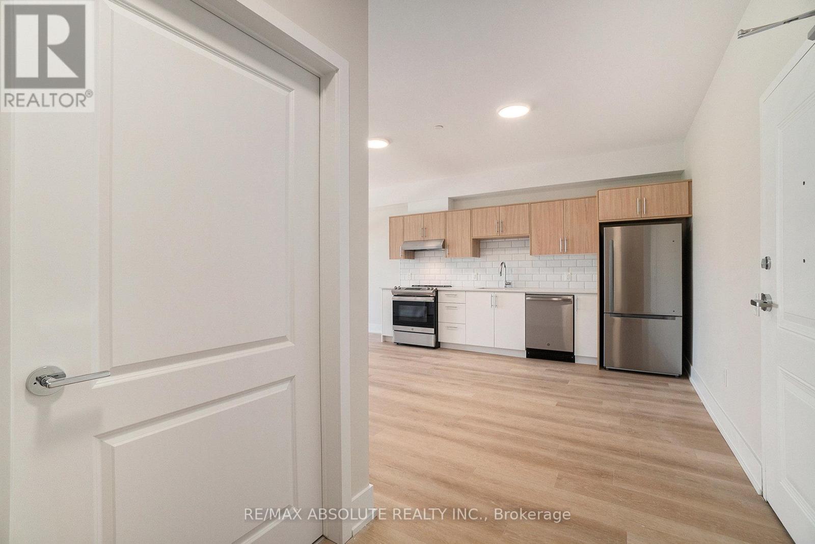 A white door opens to a kitchen with wooden floors and stainless steel appliances.