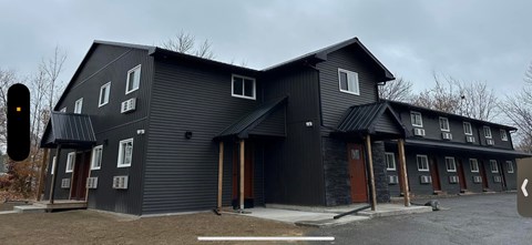 A black building with a grey roof and a white door.