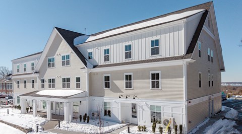 A large, modern building with a mix of beige and white siding, large windows, and a covered outdoor area.