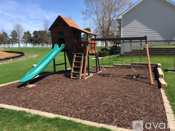 A playground with a green slide and a wooden playhouse.