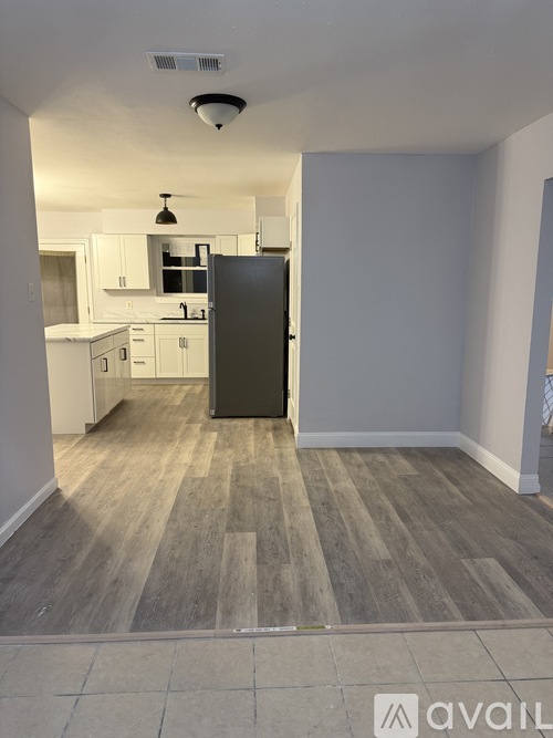 A kitchen area with a black refrigerator and wooden flooring.