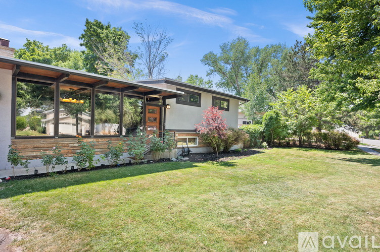 A house with a white exterior and a brown roof is surrounded by greenery.