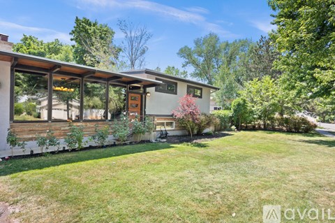 A house with a white exterior and a brown roof is surrounded by greenery.