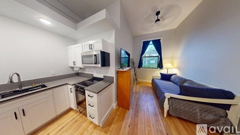 A small bedroom with a bed, a window with a view, and a kitchen area with a sink, stove, and microwave.