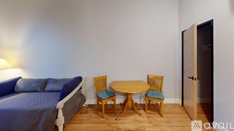 A bedroom with a bed, a table and chairs, and a door.