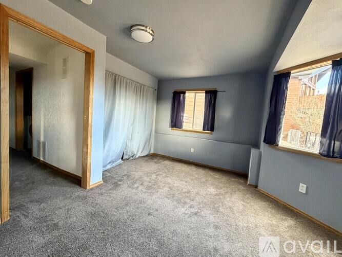 A spacious room with a grey carpet and a window with blue curtains.