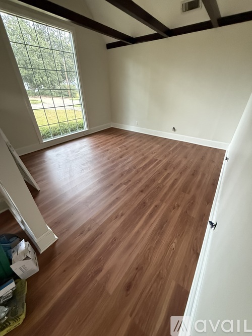 A room with wooden flooring and a window overlooking a green area.