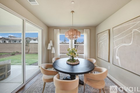 A modern dining room with a round table and chairs, a chandelier, and a view of the outdoors through a sliding glass door.