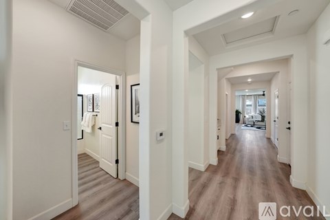 A long hallway with a door on the left and a view of a living room on the right.