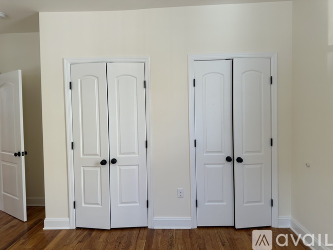 Three white doors with black handles are in a room with wood floors and white walls.