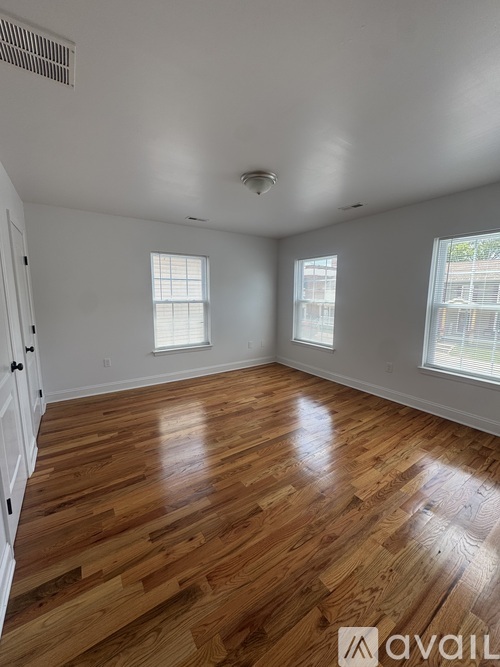 A room with wooden flooring and two windows.