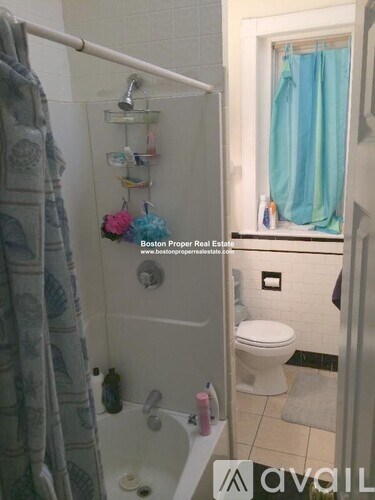A bathroom with a toilet, a shower with a blue shower curtain, and a window with a blue curtain.