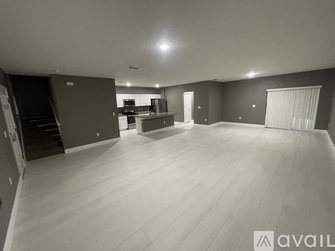 A spacious room with wooden flooring and a kitchen area in the background.