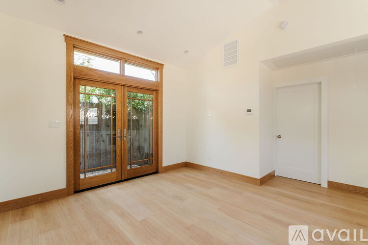 A kitchen with a refrigerator, wooden floors, and three windows.