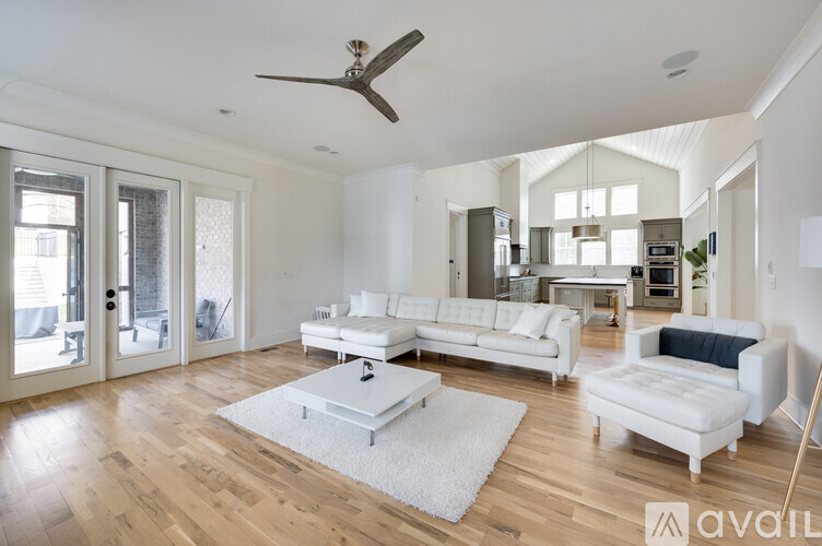 A spacious living room with a white sofa set and a wooden floor.