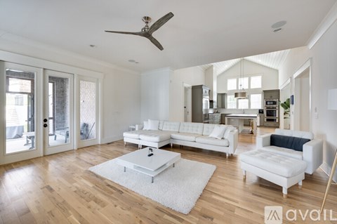 A spacious living room with a white sofa set and a wooden floor.