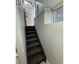 A staircase with a black carpeted runner and white walls.