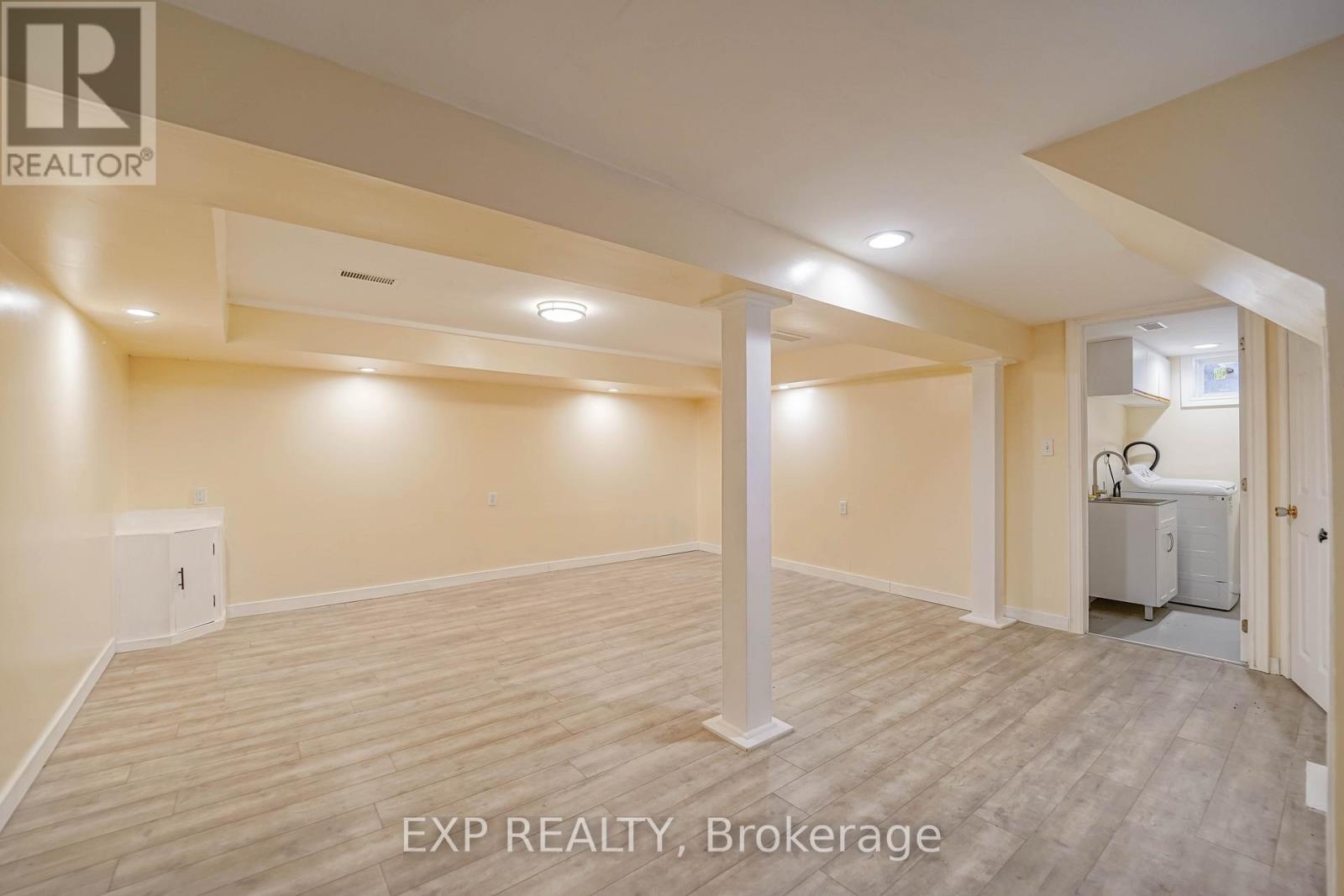 A spacious room with wooden flooring and white walls, with a pillar in the middle and a window on the right side.