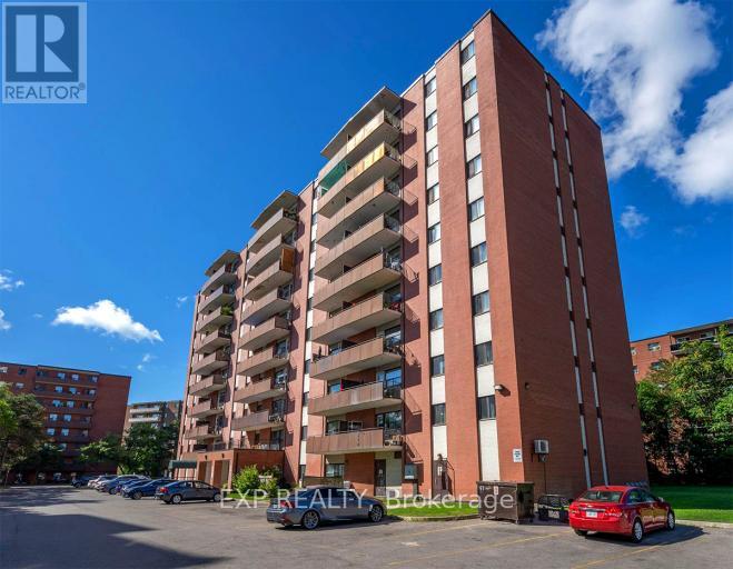 A tall red brick apartment building with a parking lot in front.
