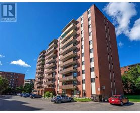 A tall red brick apartment building with a parking lot in front.