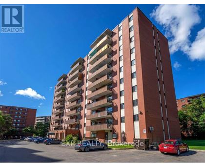 A tall red brick apartment building with a parking lot in front.