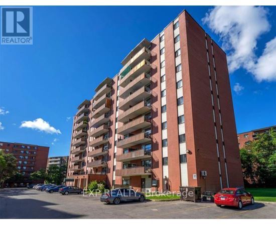 A tall red brick apartment building with a parking lot in front.