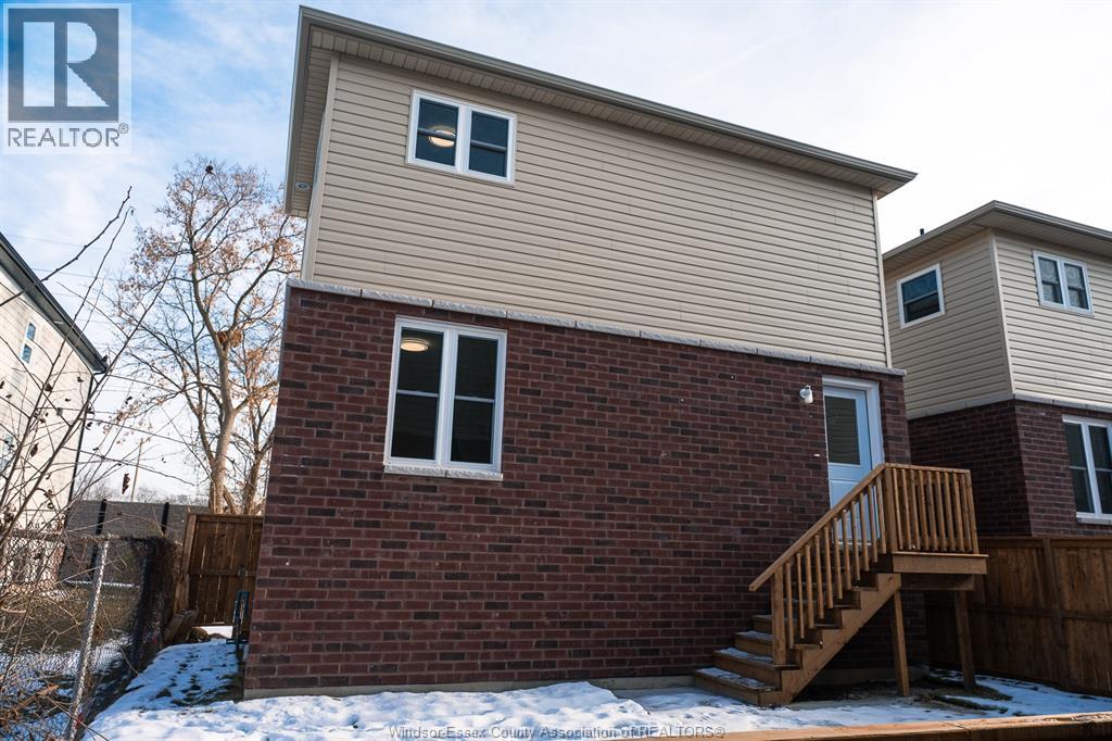 A house with a brown brick wall and a wooden staircase leading to a door.