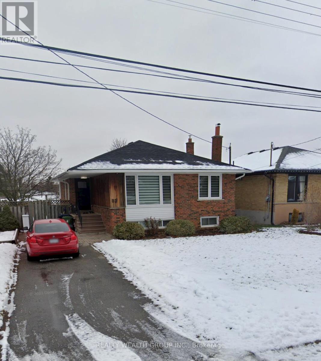 A red car is parked in front of a house with a snow-covered ground.