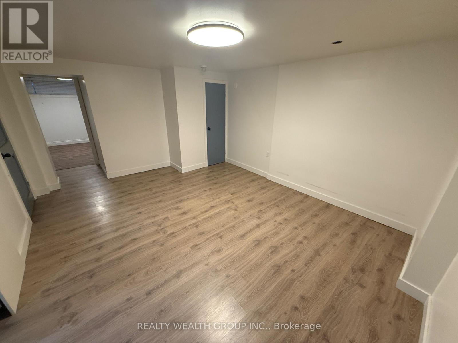 A spacious room with wooden flooring and a staircase on the left side.