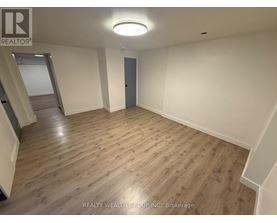 A spacious room with wooden flooring and a staircase on the left side.