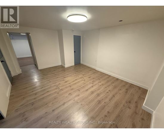 A spacious room with wooden flooring and a staircase on the left side.