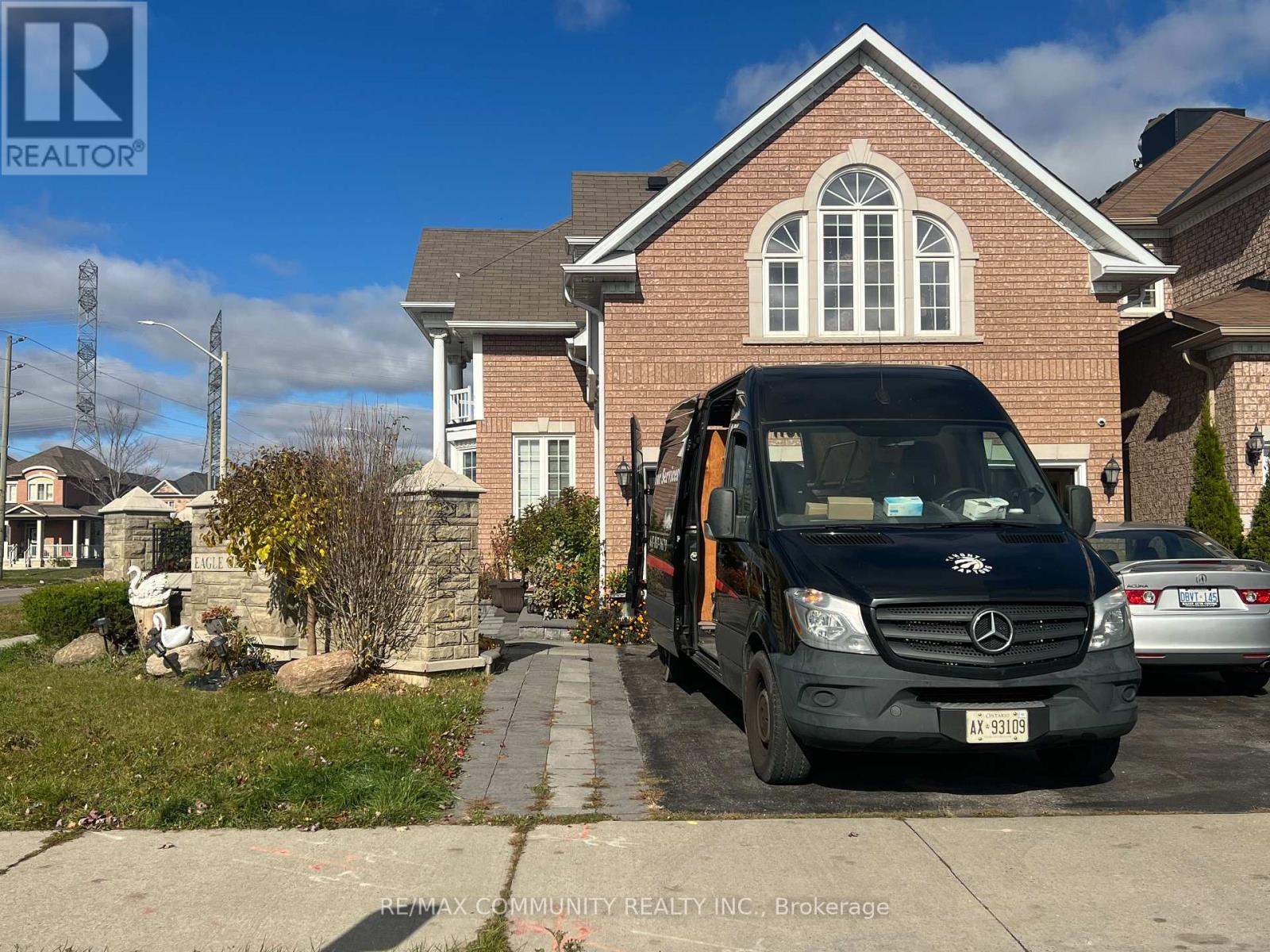 A black RE/MAX Community REALTY INC. van is parked in front of a brick house.