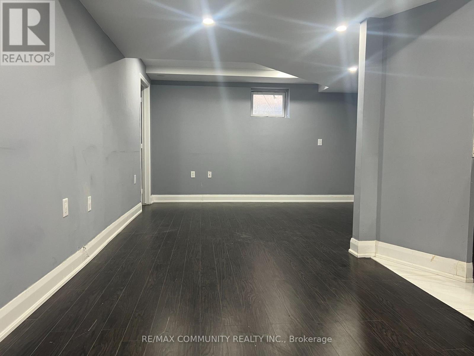 A spacious room with dark wood flooring and white walls.
