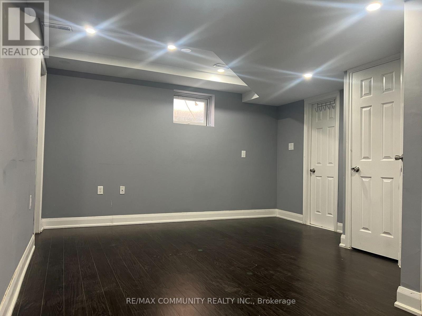 A room with grey walls and wooden flooring, with a window and two doors.