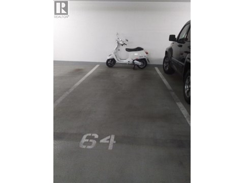 A white scooter is parked in a parking space with the number 64 painted on the ground.