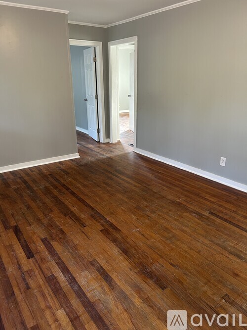 A room with wooden flooring and a doorway leading to another room.