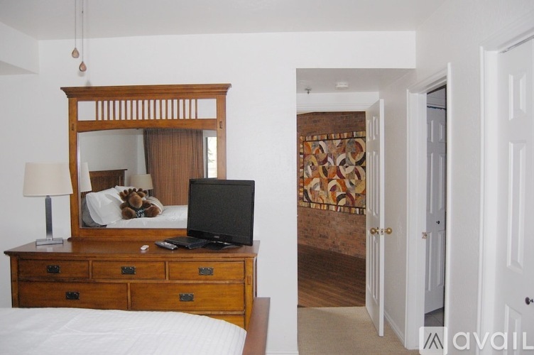 A bedroom with a bed, a desk with a laptop, and a mirror.