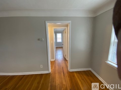 A hallway with wooden floors and white walls leading to a door.