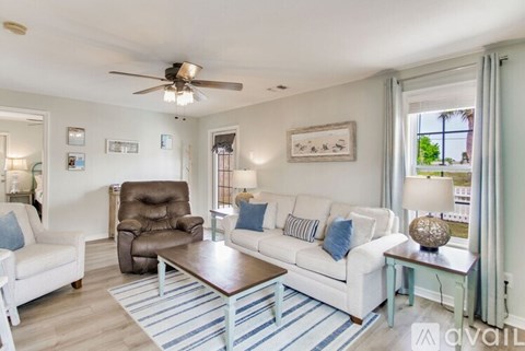 A living room with a white couch, brown chair, and a ceiling fan.