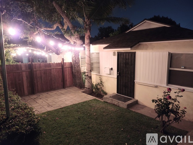A house with a fence and a tree in front of it is lit up at night.