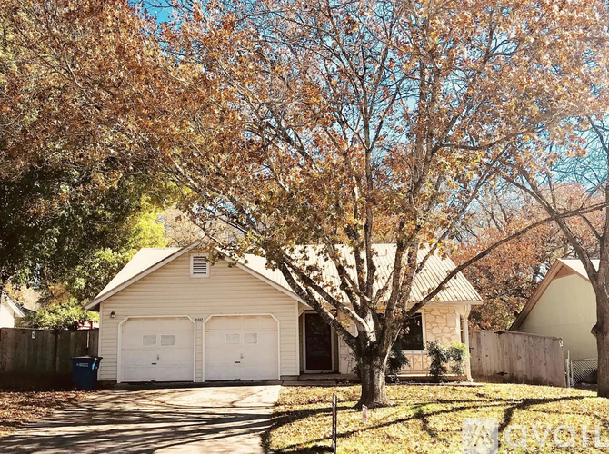 A house with a white garage door is surrounded by trees with yellow leaves.