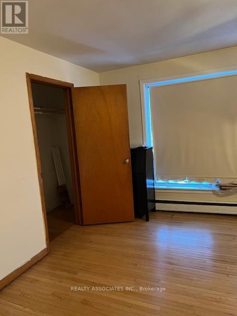 A room with a wooden floor, a brown door, and a window with blinds.