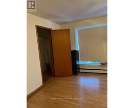 A room with a wooden floor, a brown door, and a window with blinds.