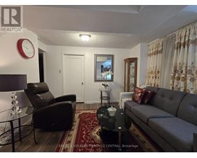 A living room with a grey couch, a black chair, and a red rug.