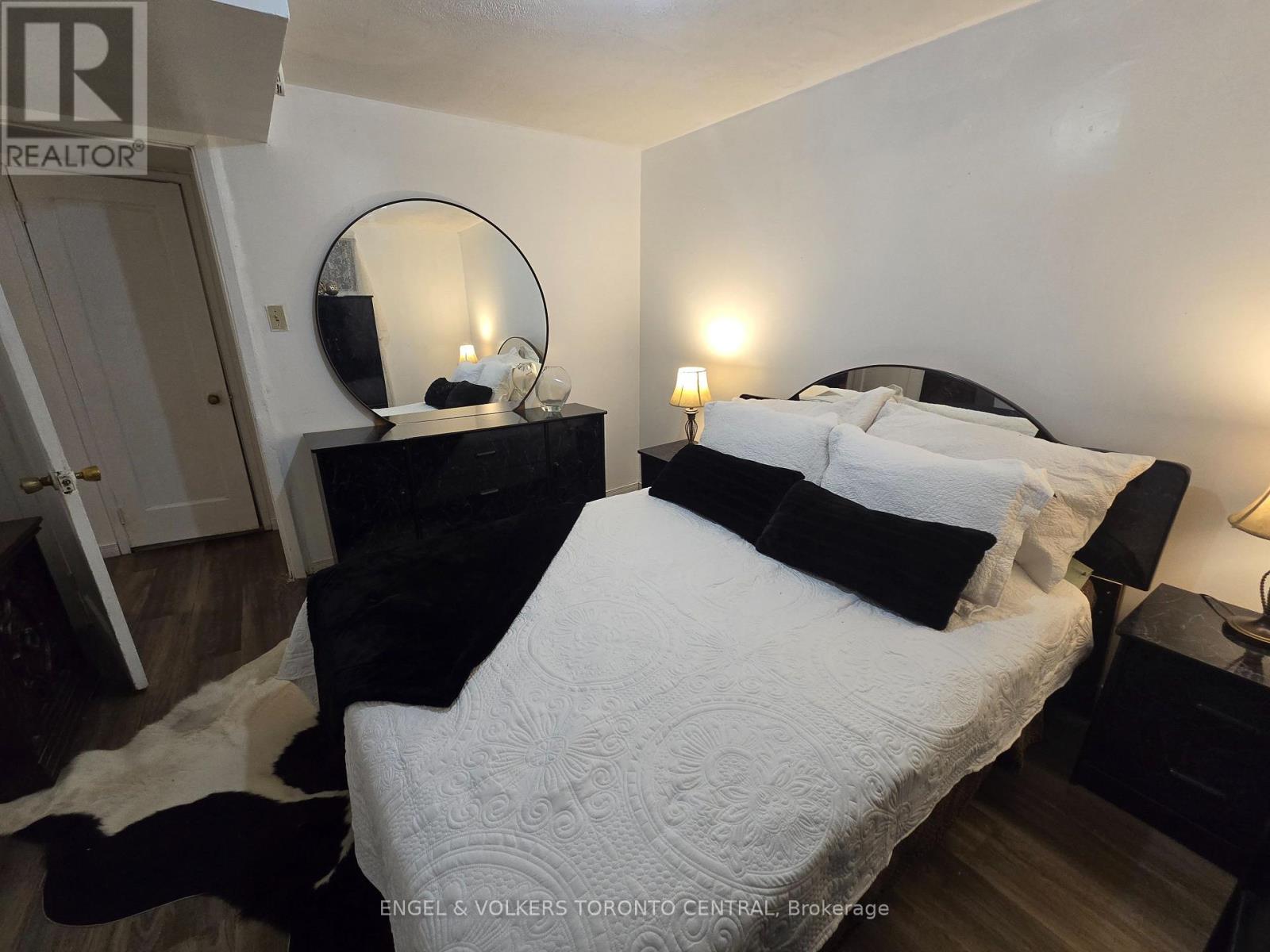 A bedroom with a large bed and a mirror on the dresser.