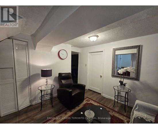 A living room with a black leather chair and a glass table with a vase of flowers on it.