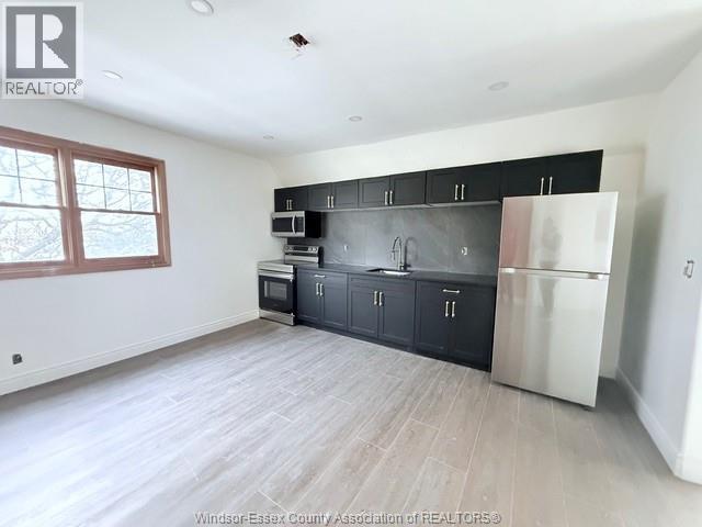 A kitchen with black cabinets and a stainless steel refrigerator.