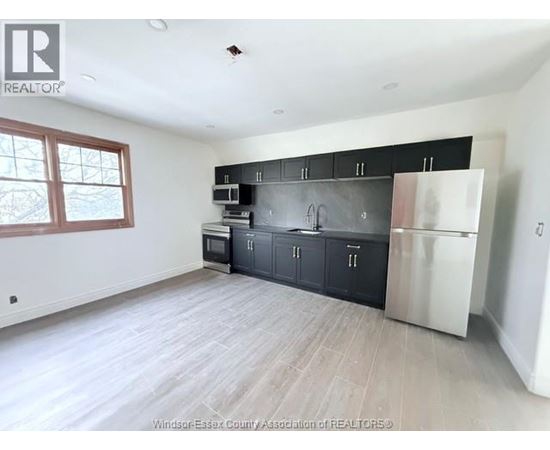 A kitchen with black cabinets and a stainless steel refrigerator.