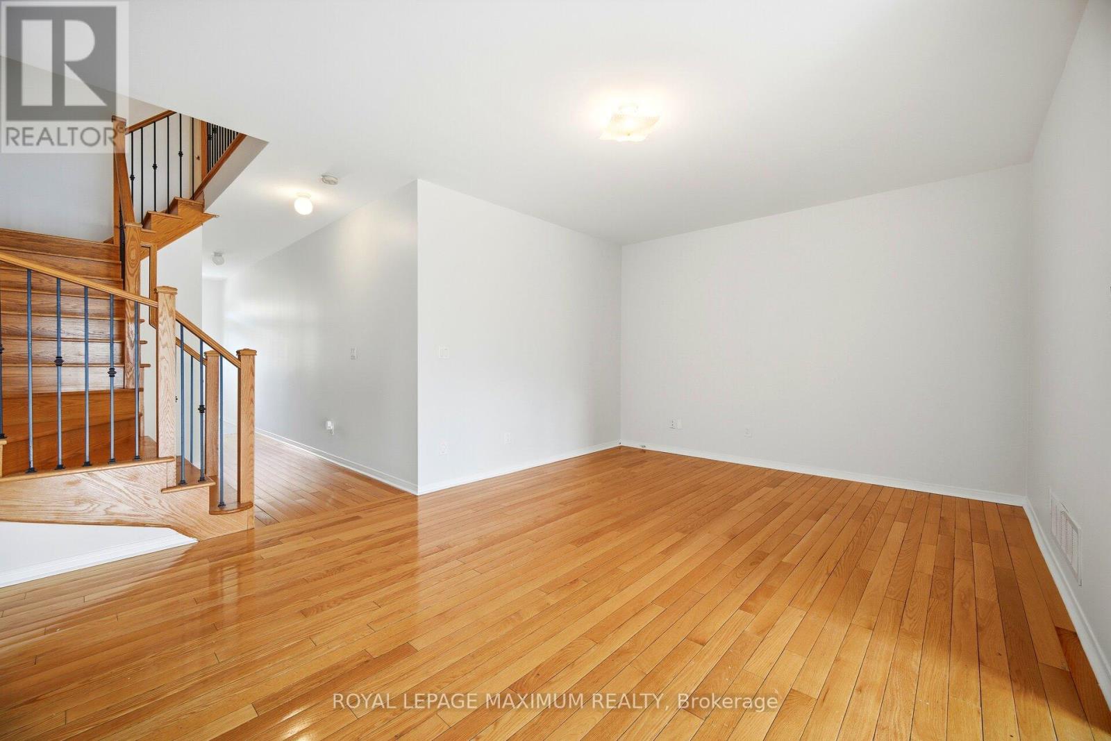 A spacious room with wooden flooring and a staircase on the left side.